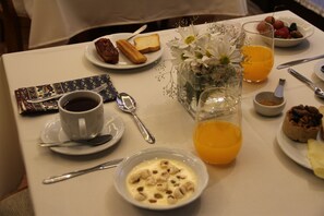 Una mesa de desayuno con una taza de café, un tazón de cereal, tostadas, un vaso de jugo de naranja y un pequeño florero con flores.