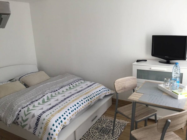 A bedroom with a bed, a desk, a chair, a TV, and a water bottle on the desk.