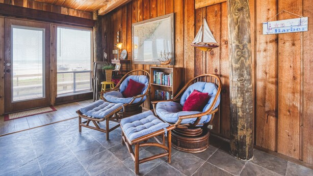 A cozy room with wooden walls and ceiling, two wicker chairs with cushions, a bookshelf, and a sign reading "Harbor". - Toes In The Sand Drink In My Hand (Freeport)