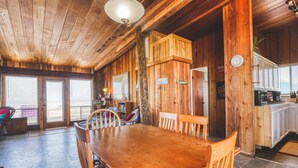 A wooden interior with a dining table and chairs, a kitchen area, and a large window. - Toes In The Sand Drink In My Hand (Freeport)