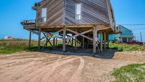 A two-story wooden house elevated on stilts, with a sign indicating it is for rent. - Toes In The Sand Drink In My Hand (Freeport)