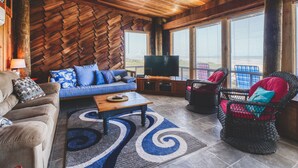 A cozy living room with a wooden ceiling, a sofa with blue cushions, a coffee table, and wicker chairs. - Toes In The Sand Drink In My Hand (Freeport)