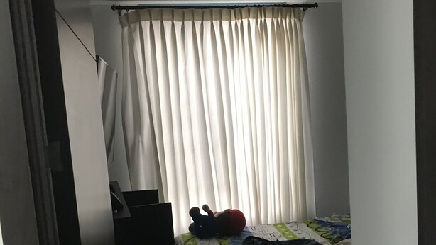 Une petite pièce faiblement éclairée, avec un lit simple, une petite table et un rideau.