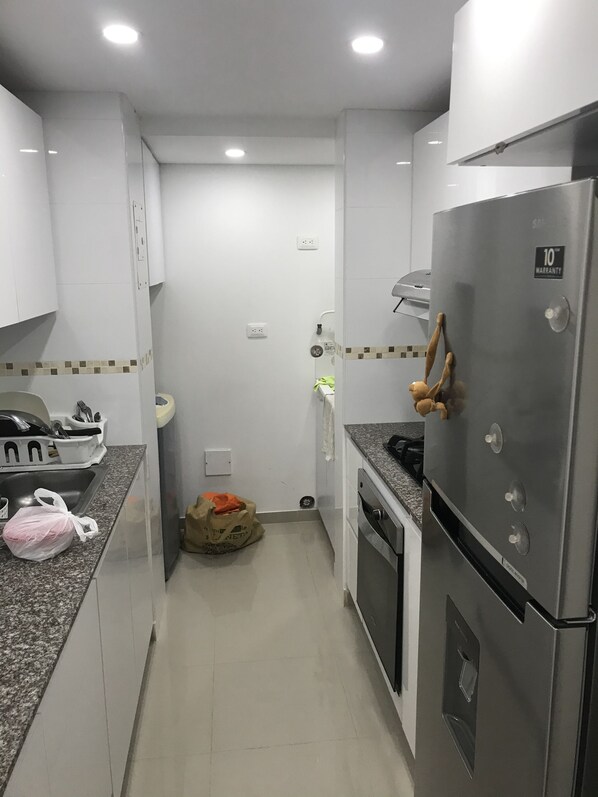 Una cocina compacta con armarios blancos, un refrigerador de acero inoxidable y un lavamanos.