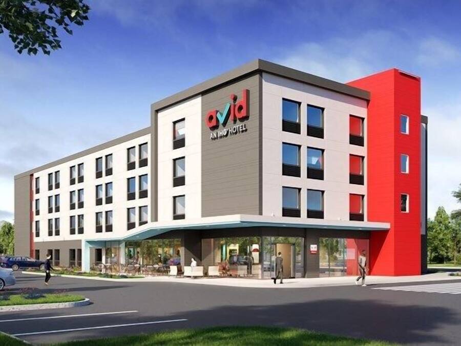 Un hotel moderno con una fachada destacada en rojo y gris, varios pisos y una zona de entrada cubierta.