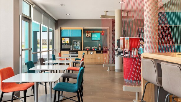 A modern restaurant with multiple tables and chairs, a counter area, and large windows allowing natural light.
