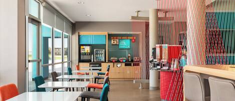 A modern restaurant with multiple tables and chairs, a counter area, and large windows allowing natural light.