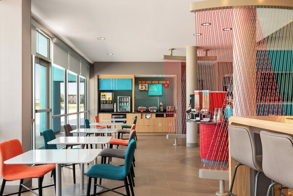 Un restaurant moderne doté de nombreuses tables et chaises, d’un comptoir et de grandes fenêtres laissant entrer la lumière naturelle.