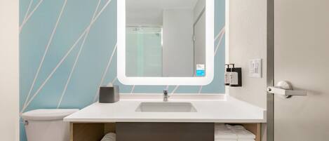 A bathroom with a white sink, a mirror with a light, a toilet, and a towel rack with towels.