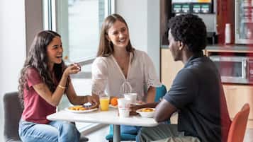 Three people seated at a table with breakfast items, in a room with a window and a microwave in the background.