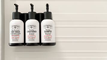 Three J.R. Watkins products: body wash, conditioner, and shampoo, displayed on a white wall.