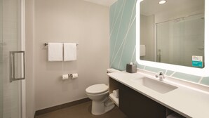 Un baño moderno con cabina de ducha de vidrio, inodoro blanco, tocador con espejo y un perchero para toallas.