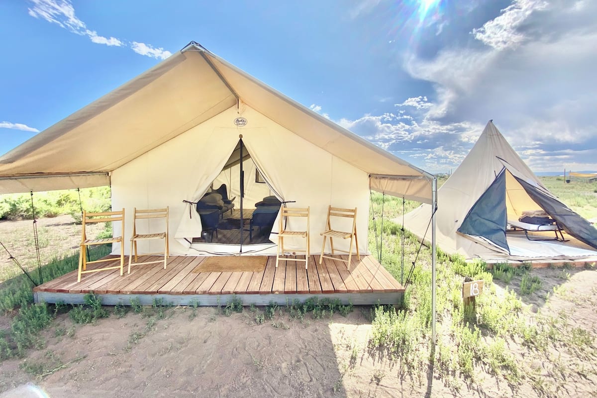 A tent with a wooden deck and two chairs, set in a natural landscape.