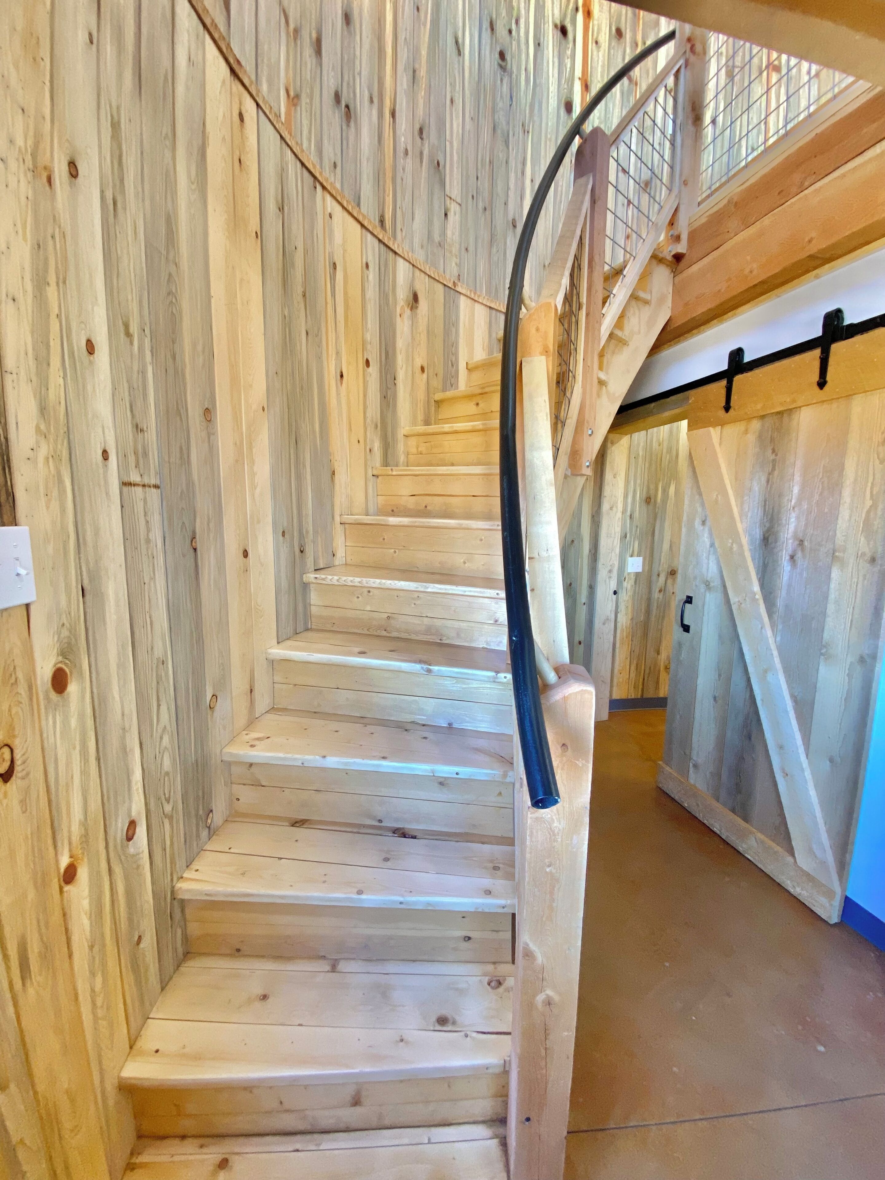 Un escalier en bois avec une rampe métallique et un mur en bois avec une balustrade métallique.