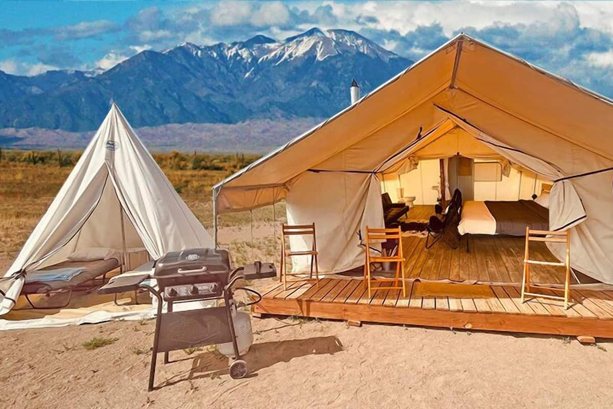 Two tents with a wooden deck and seating area, set against a mountainous backdrop.