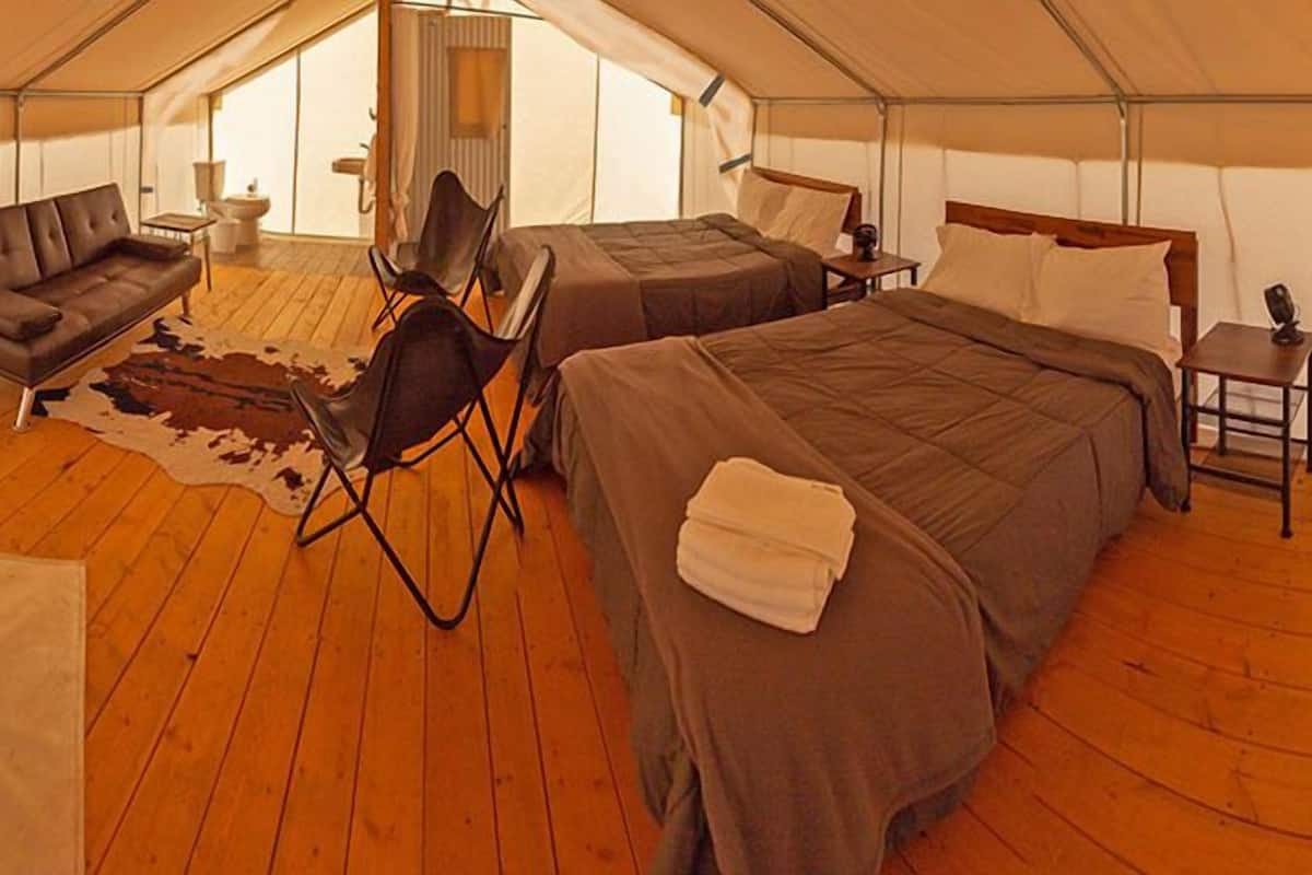 A tented accommodation with two beds, a sofa, a chair, and a small table.
