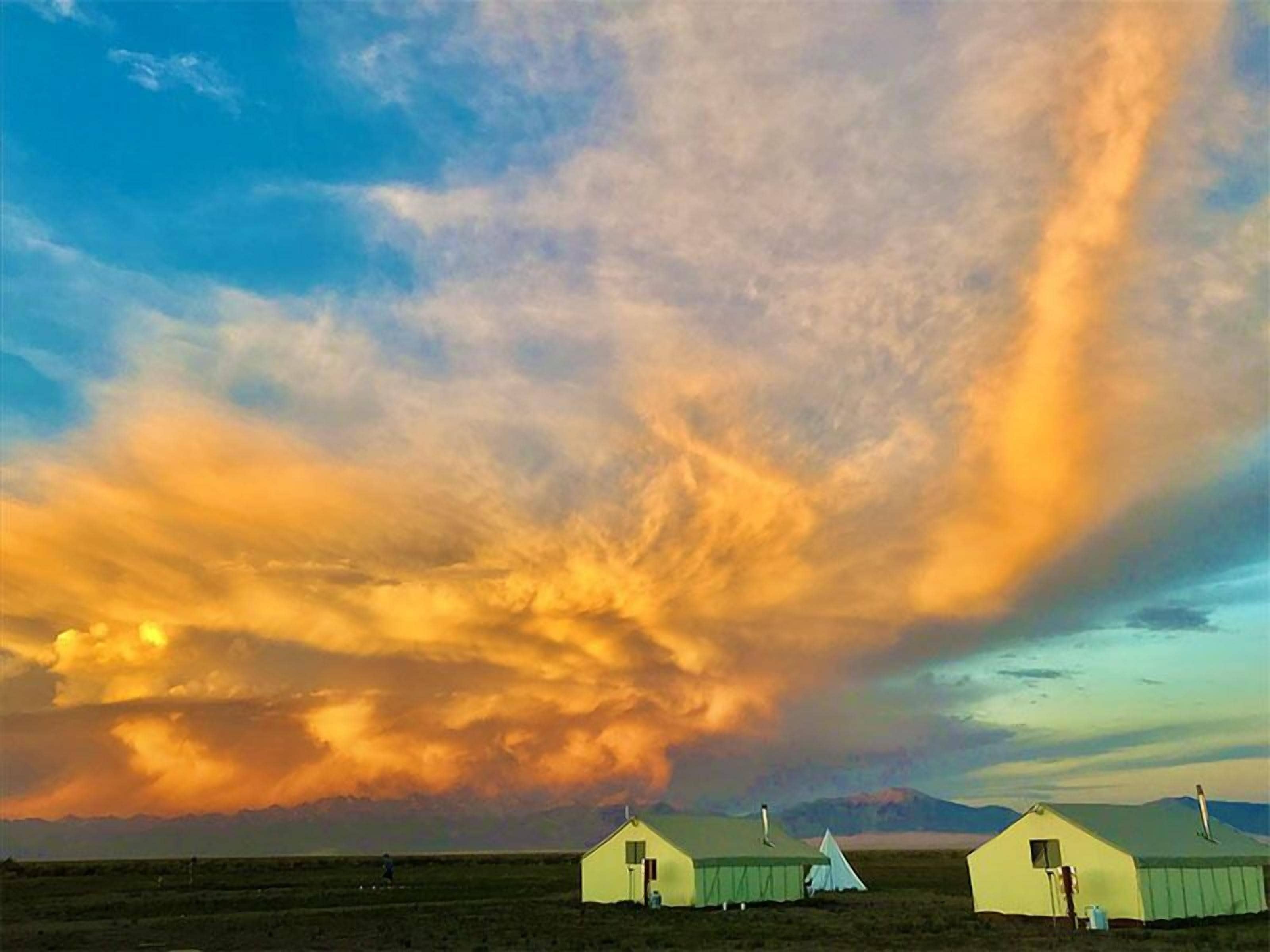 A landscape with a clear sky, a large cloud formation, and three yurts.