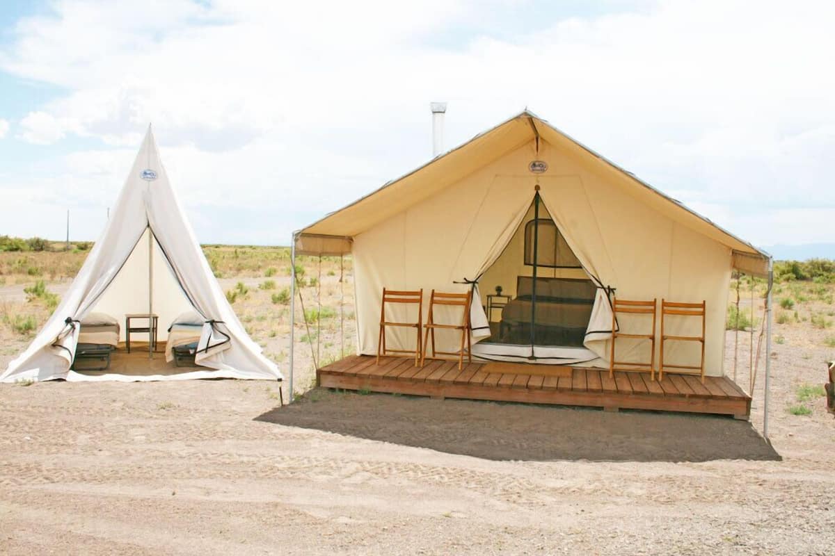 A tent with a wooden deck and seating area, a smaller tent nearby, and a clear sky.