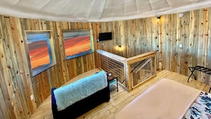Une pièce aux murs en bois, avec un canapé, un lit, une cheminée et deux tableaux.