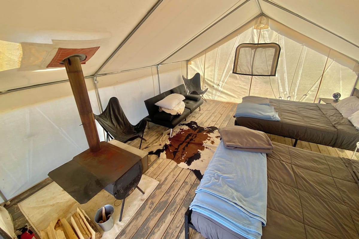 A tent interior with a bed, a chair, a small table, and a stove.