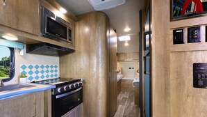 Une cuisine compacte équipée d’une cuisinière, d’un four à micro-ondes et d’un évier, ainsi qu’un petit espace nuit comprenant un lit et des toilettes.