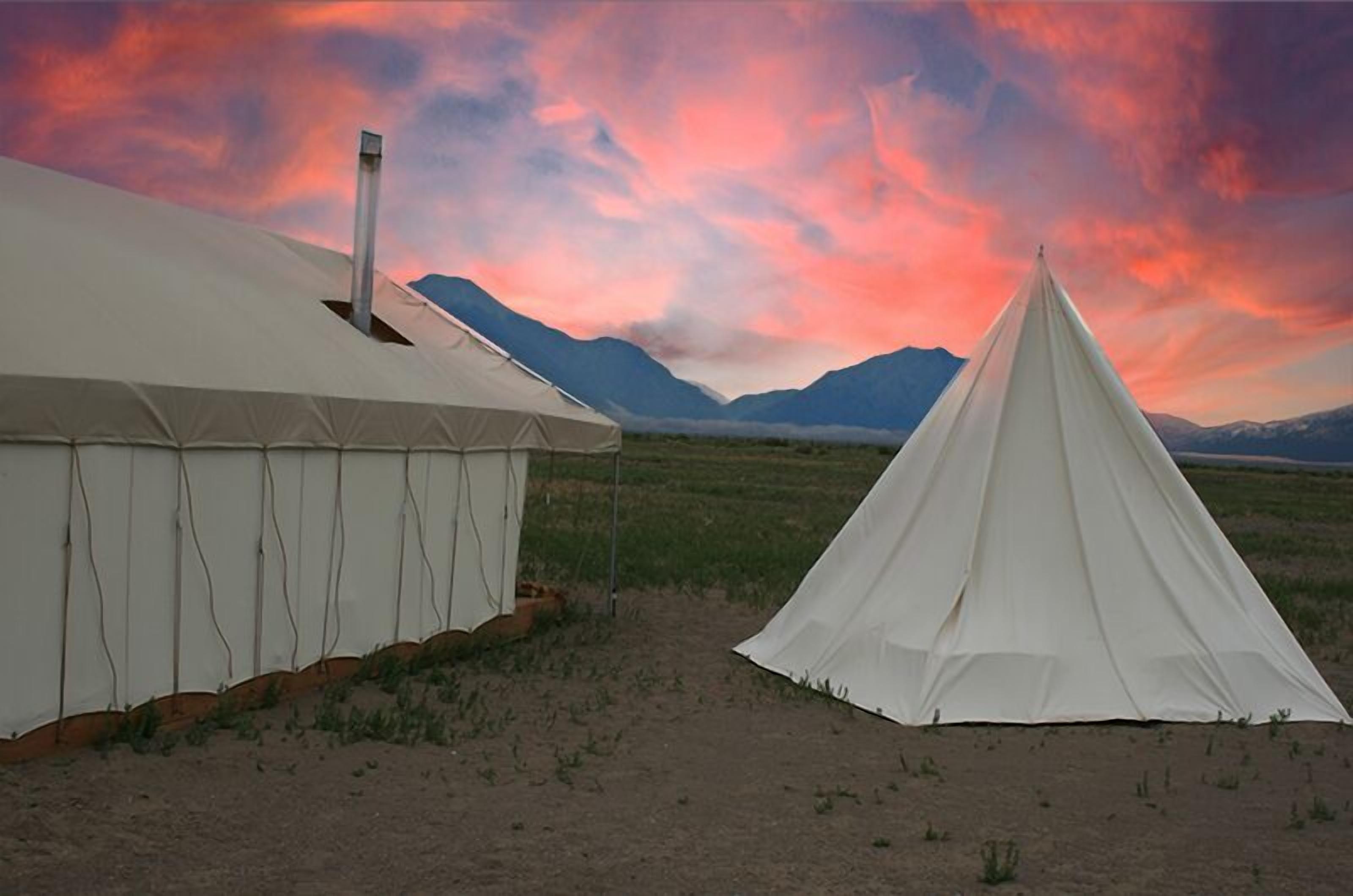 Two white tents in a desert landscape with mountains in the background.