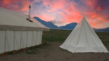 Two white tents in a desert landscape with mountains in the background.