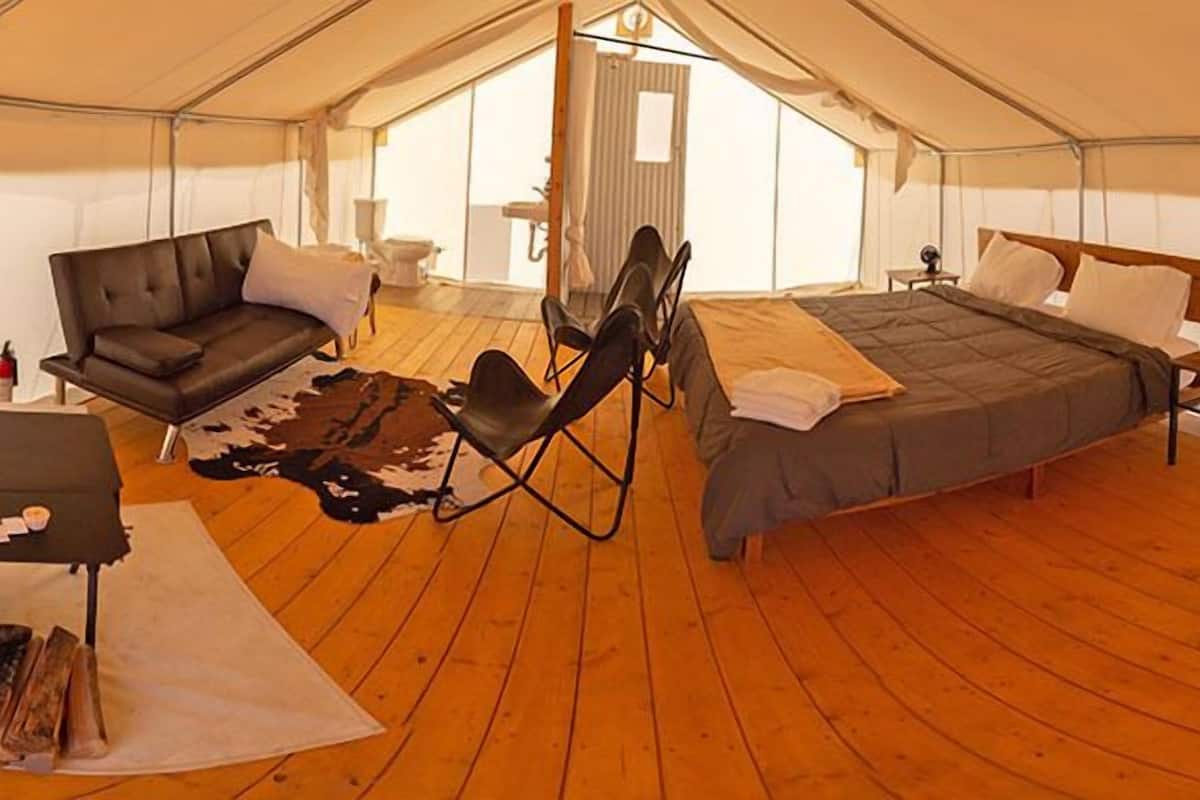 A tented room with a bed, a sofa, a chair, and a small table.