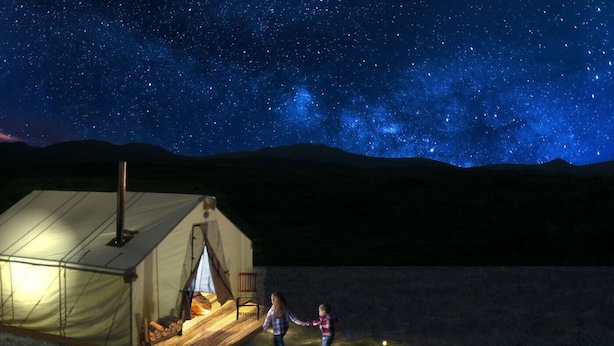 Un hébergement sous tente offrant une vue imprenable sur le ciel étoilé, avec une cheminée à l’intérieur et un enfant qui joue à l’extérieur.