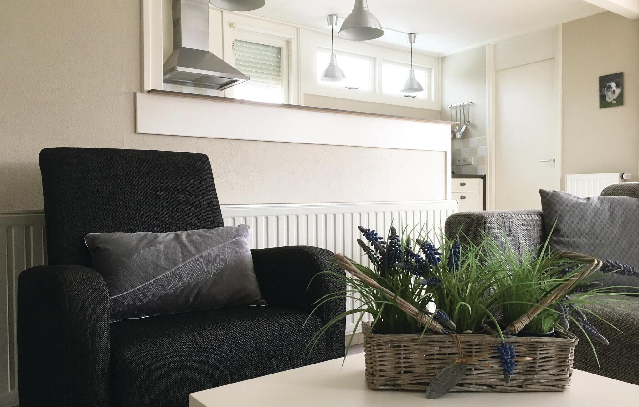 Un salon avec un fauteuil sombre, une table blanche et un panier en osier contenant des plantes.