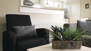 A living room with a dark armchair, a white table, and a wicker basket with plants.