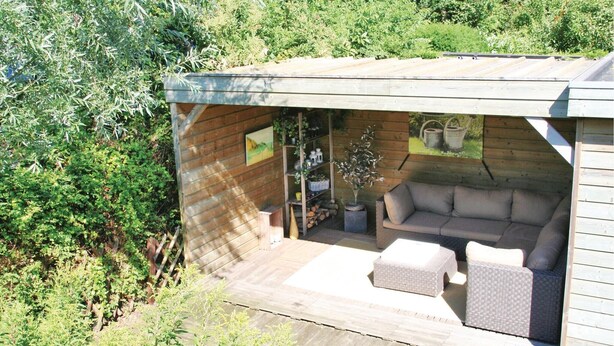 A wooden deck with a sofa and cushions, surrounded by greenery.