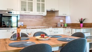 A modern kitchen with white cabinets, a wooden countertop, and a dining table set with chairs and wine glasses. - Lovely home in Puljane (Puljane)