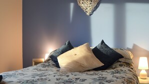 Una cama con ropa de cama estampada con motivos florales, una decoración de pared con forma de corazón y una lámpara de noche.