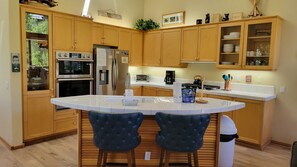 A modern kitchen with wooden cabinets, a built-in oven, a refrigerator, and a central island with bar stools.