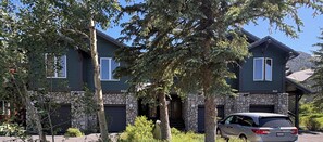 A two-story house with stone facade and a garage, surrounded by trees and a parked car. - Snowcreek Resort Vacation Rental 955 (Mammoth Lakes)