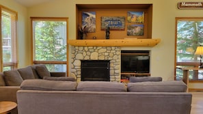 A living room with a stone fireplace, a large flat-screen TV, and a couch. - Snowcreek Resort Vacation Rental 955 (Mammoth Lakes)