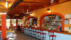 Uma área de bar com vários bancos e um balcão, rodeada por vigas de madeira e paredes laranja.