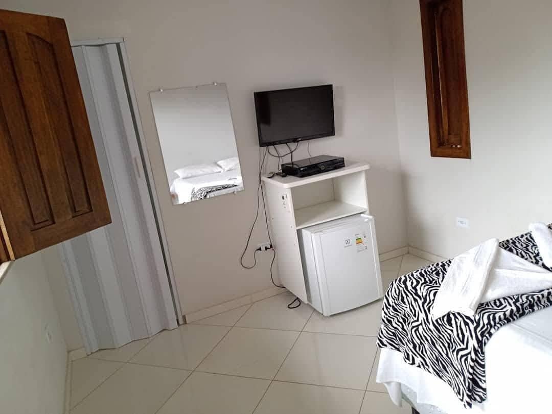 Ein Schlafzimmer mit einem Bett, einem an der Wand befestigten Fernseher, einem kleinen, weißen Kühlschrank und einem Spiegel.
