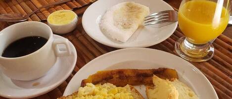 Un desayuno con tostadas, huevos revueltos y jugo de naranja sobre un tapete de bambú.