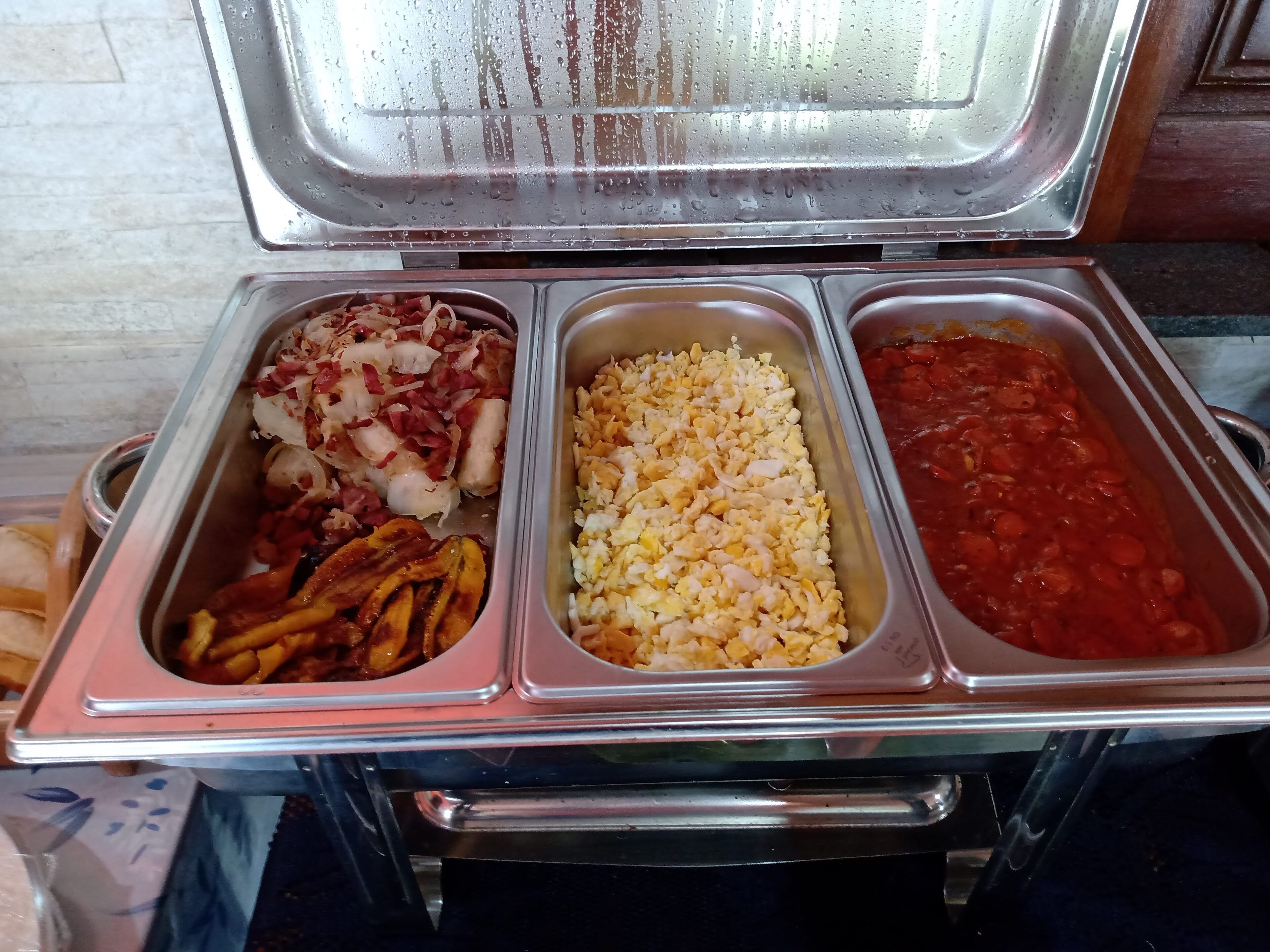 Un buffet avec trois plateaux de nourriture : un avec du bacon et des oignons, un avec des œufs brouillés et un avec du chili.