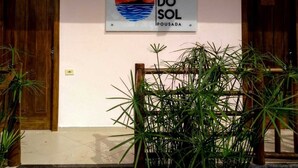 A sign with a sunset and palm trees, a wooden door, and a plant in the foreground. - Pousada Pôr do Sol (Maraú)