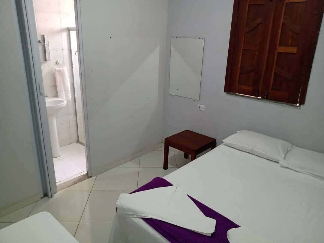 A bedroom with a bed, a small wooden table, a whiteboard, and a shower area.