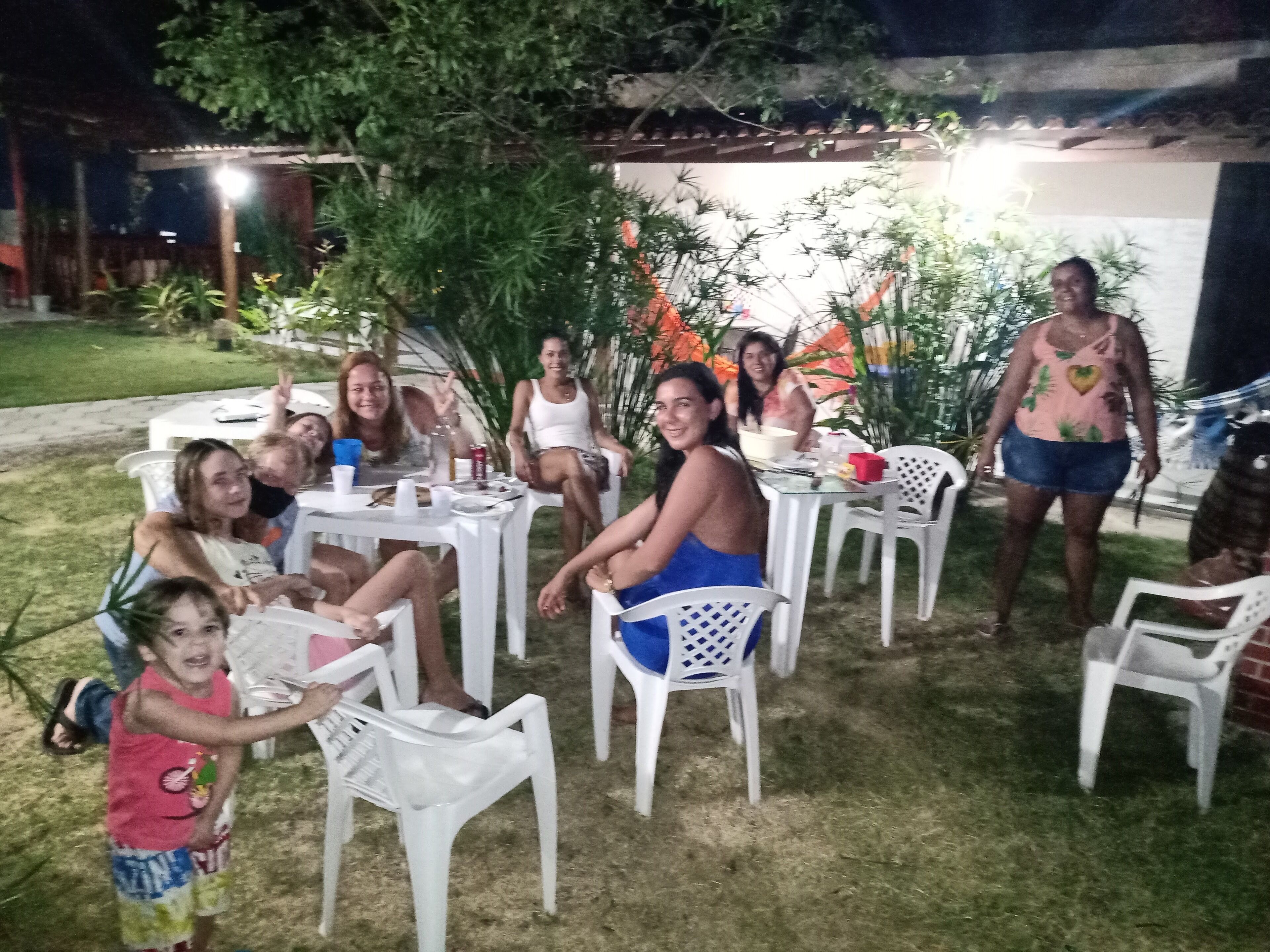 A group of people seated at tables outdoors with a garden in the background.