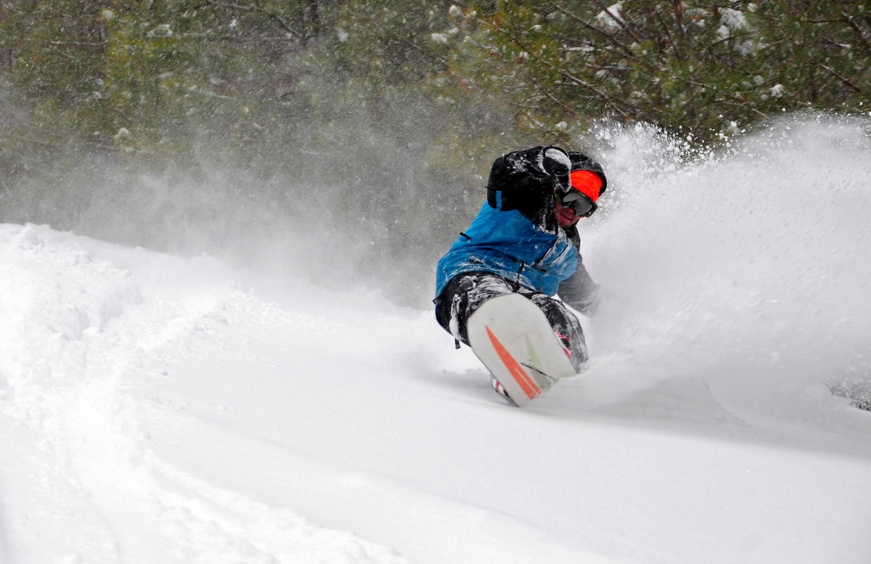 A snowboarder in a blue jacket and helmet navigating a snowy slope.