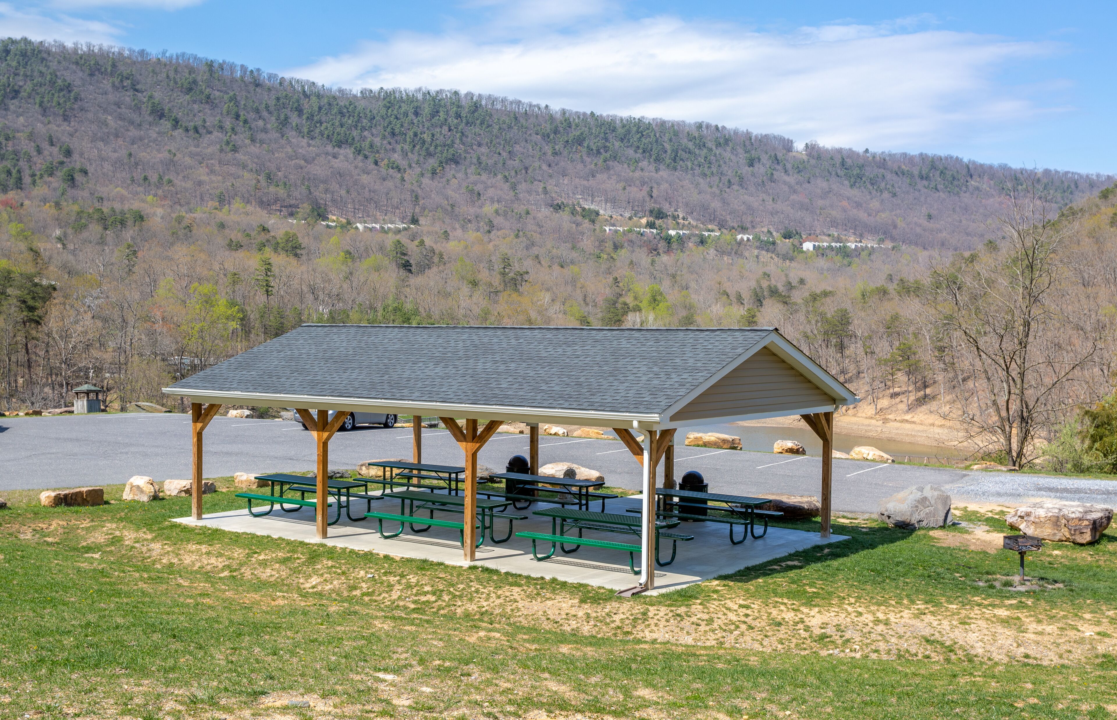 A covered picnic area with benches and picnic tables, set against a backdrop of a hilly landscape.