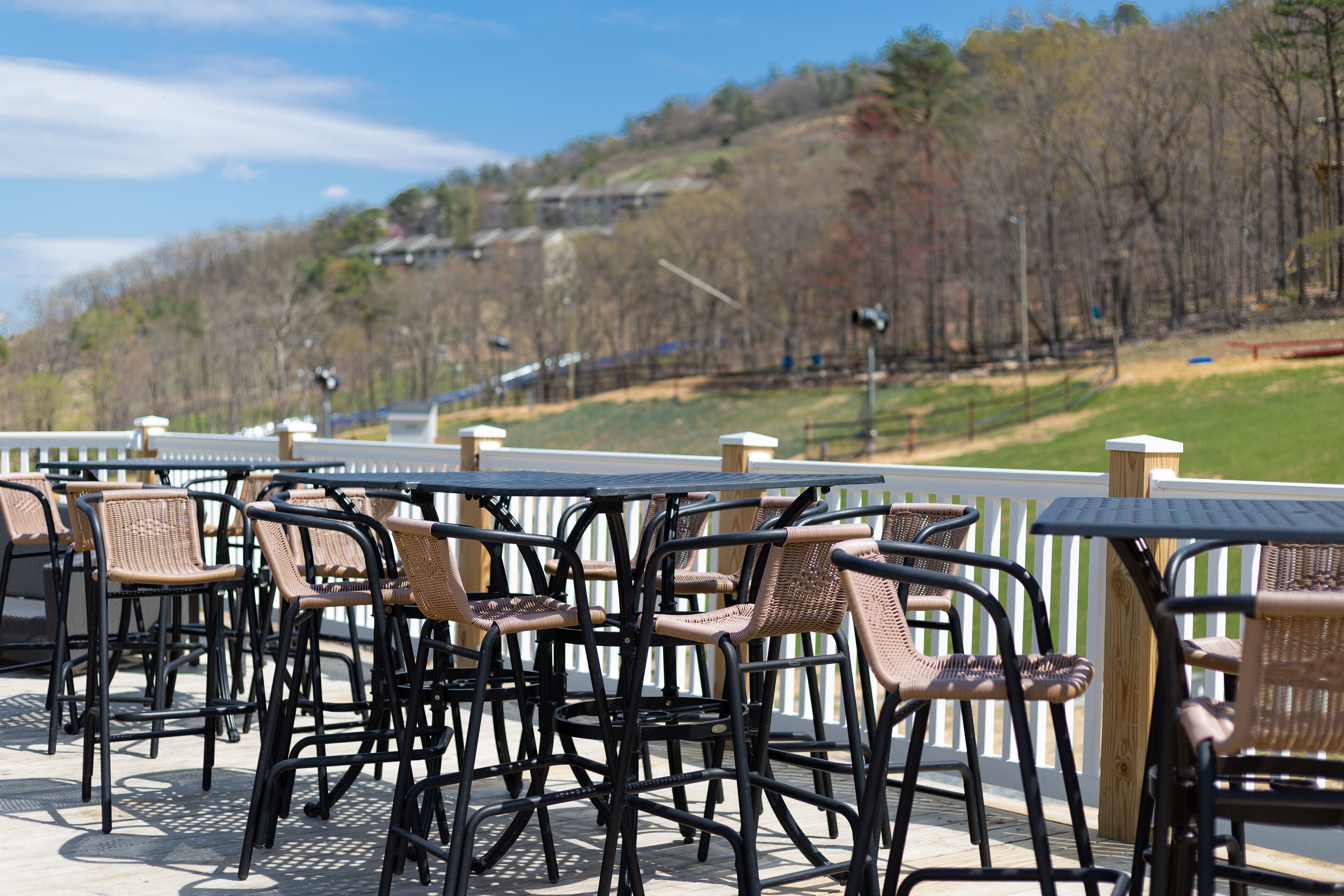 Eine Terrasse im Freien mit Korbstühlen und Tischen, mit Blick auf eine hügelige Landschaft mit Bäumen und blauem Himmel.