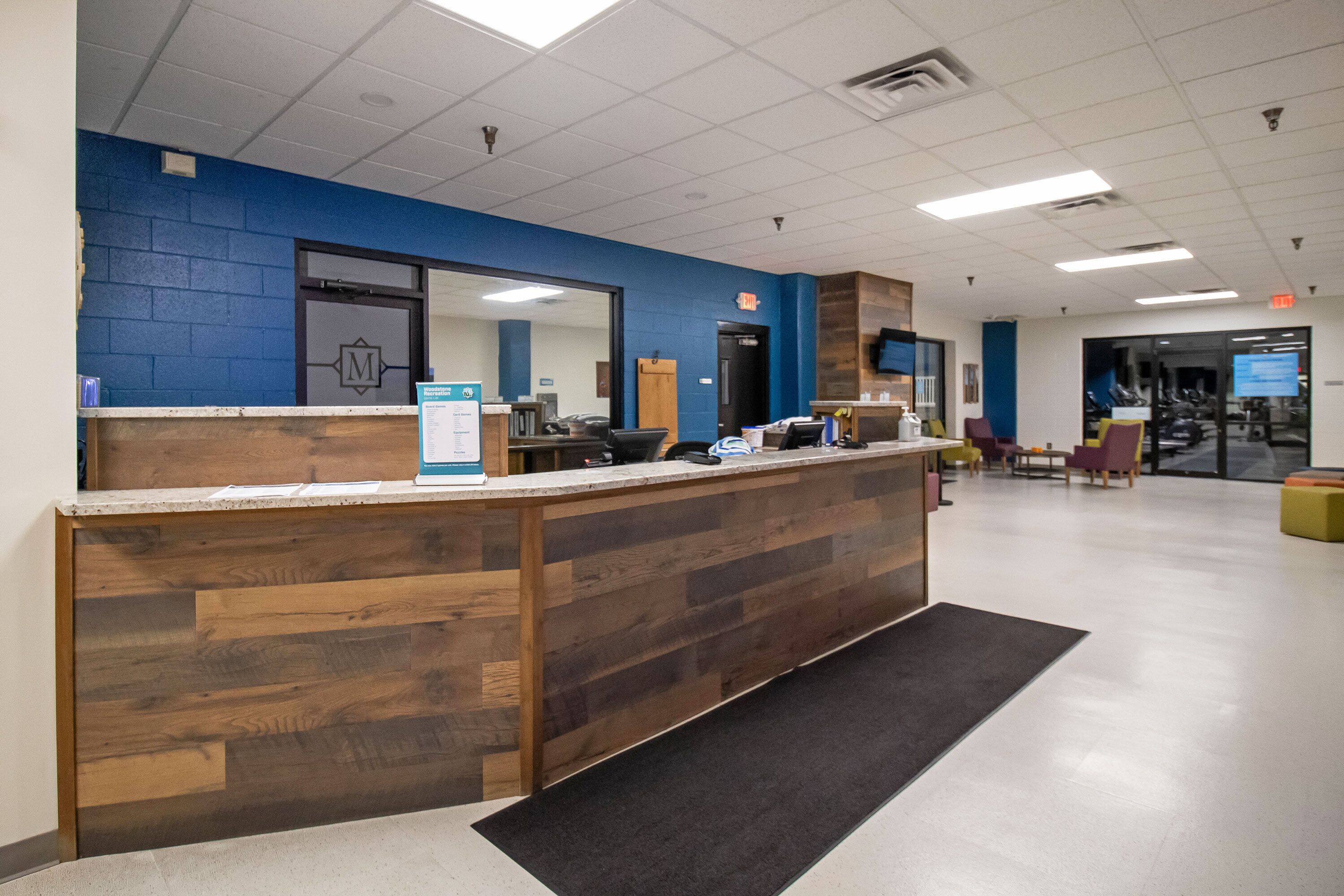A reception desk with a blue wall and a wooden counter, a sign for Woodstow Recreation, and a door with an exit sign.