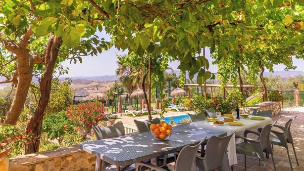 Een terras met een eettafel gedekt voor twee personen, omringd door stoelen, en een schaal fruit op de tafel.