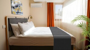 A neatly made bed with a headboard, a bedside lamp, a large abstract painting on the wall, and a potted plant by the window.